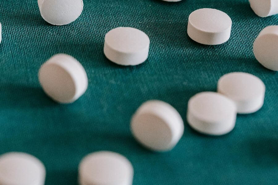Pastillas blancas dispersas sobre una tela verde, representando la medicación convencional y su relación con las terapias complementarias