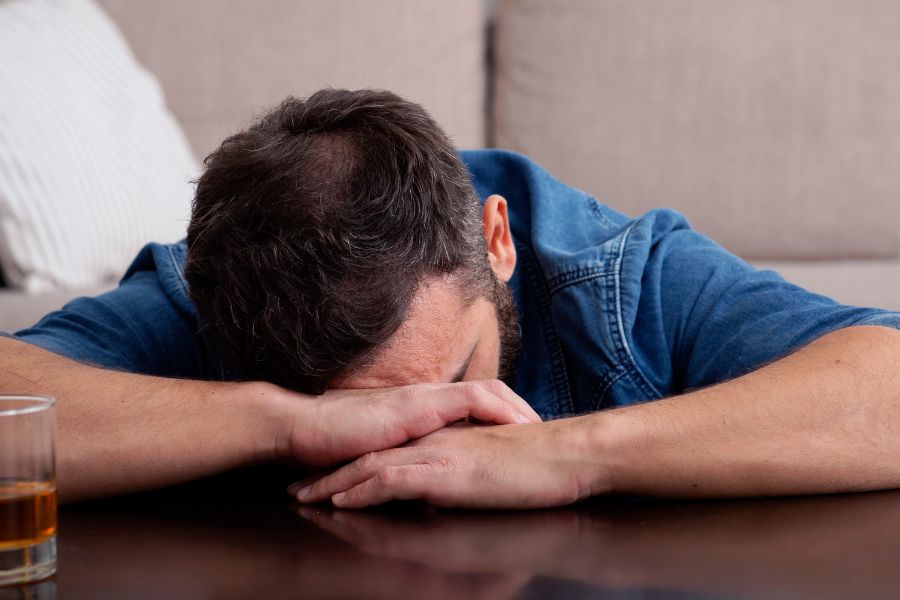 Hombre con el rostro apoyado sobre la mesa, reflejando agotamiento emocional y el peso de un consumo ligado a heridas familiares no resueltas.