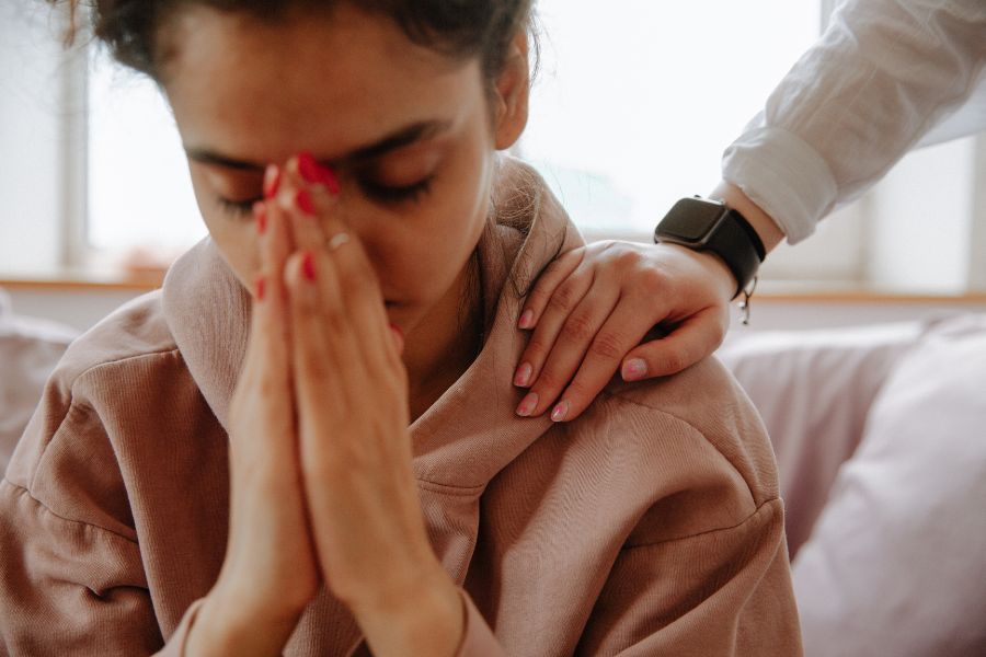 Mujer conmovida con una mano sobre su hombro, simbolizando la necesidad de contención emocional en contextos familiares desorganizados donde la adicción surge como refugio.