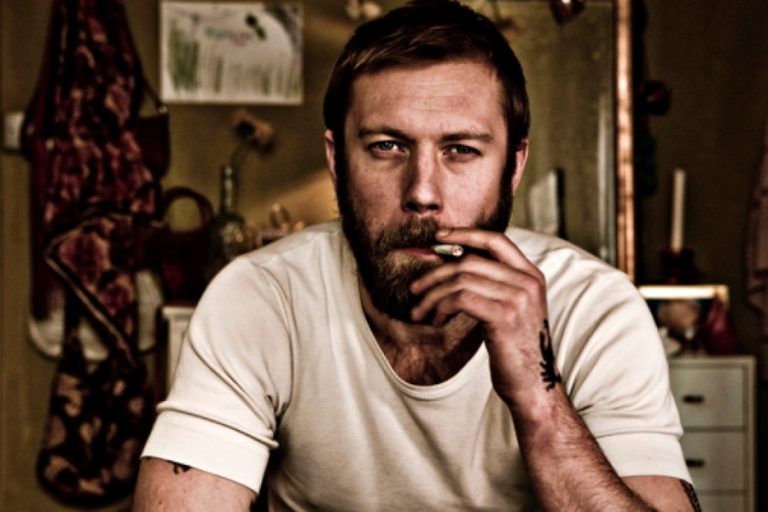 Protagonista de la película Submarino, fumando, reflejando su lucha interna y las heridas emocionales profundas que aborda la historia.