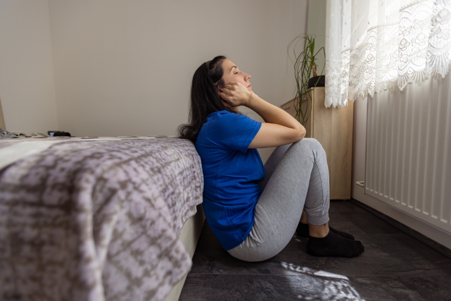 Mujer sentada en el suelo junto a la cama, con expresión de angustia y postura rígida, representando un estado de congelación.