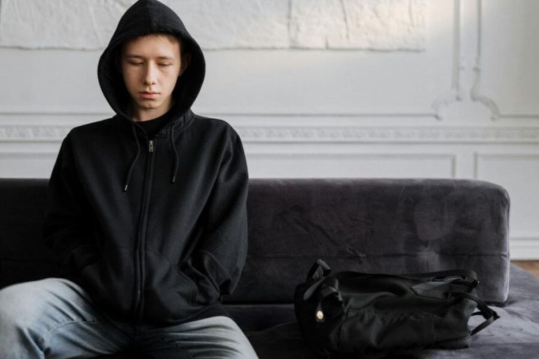 Adolescente con sudadera negra sentado en un sofá, reflejando soledad y desconexión emocional, concepto de infancia vacía.