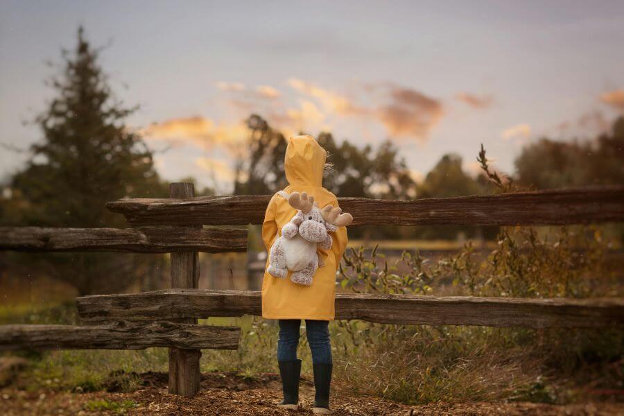 Niño con abrigo amarillo y peluche mirando el horizonte, simbolizando la infancia vacía y la soledad infantil.