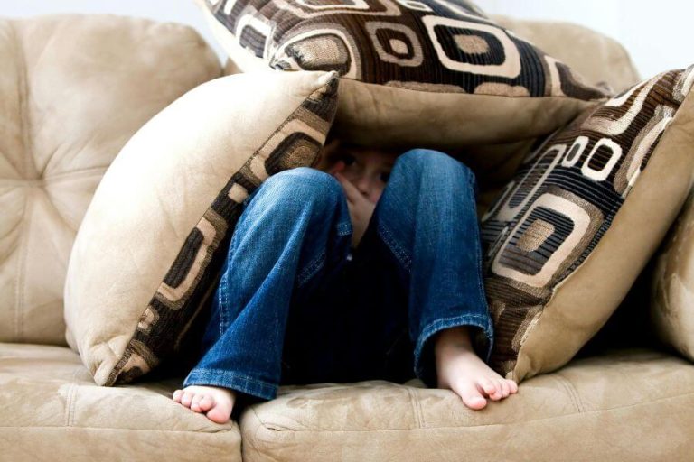 Niño escondido entre cojines en un sofá, simbolizando el trauma infantil y el miedo en la infancia