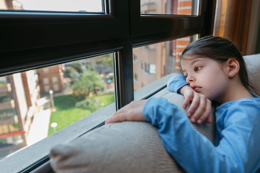 Niña apoyada junto a una ventana con expresión triste, reflejando señales emocionales asociadas al abuso infantil.