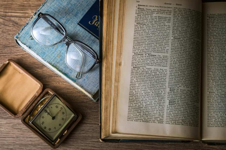 Libros antiguos, gafas y un reloj como representación del paso del tiempo y la transmisión del trauma transgeneracional.