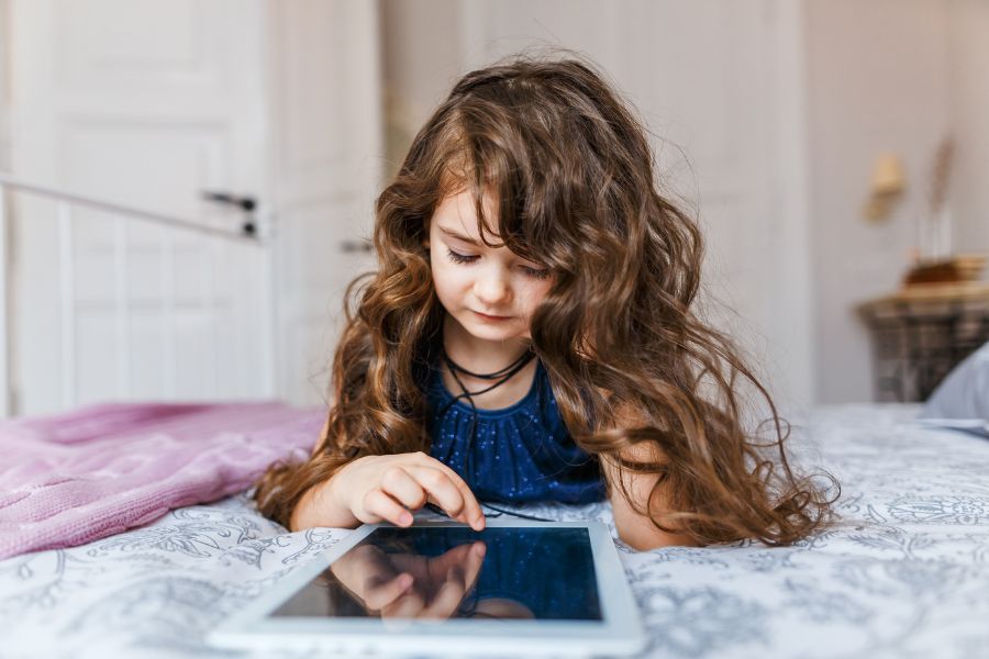 Niña utilizando una tablet en su habitación, destacando la importancia de la seguridad digital para prevenir el ASI.