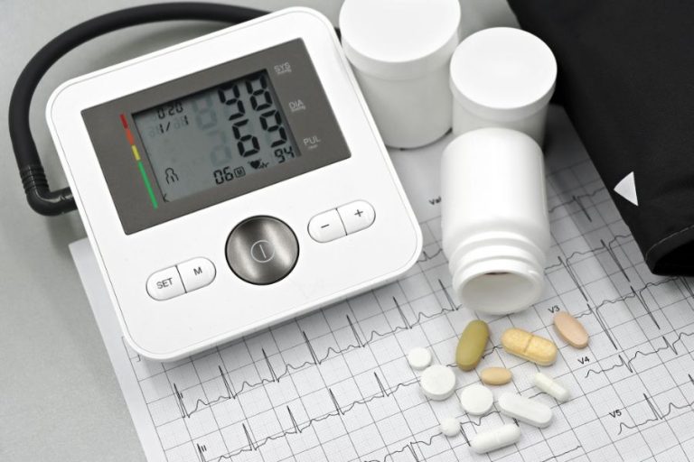 Tensiómetro digital y medicamentos sobre un electrocardiograma, representando enfermedades cardíacas e hipertensión que aumentan en Navidad.