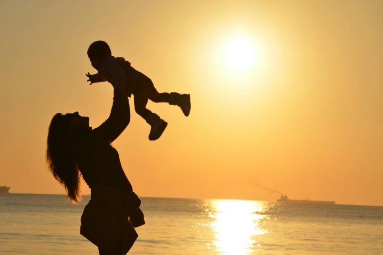 Madre levantando a su bebé frente al atardecer, simbolizando el vínculo temprano y la conexión con la niña interior.