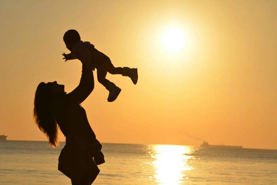 Madre levantando a su bebé frente al atardecer, simbolizando el vínculo temprano y la conexión con la niña interior.