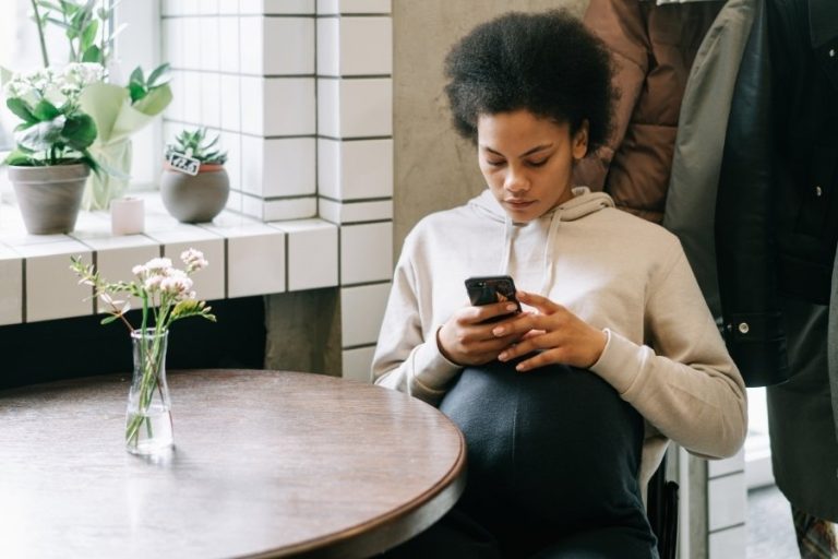 Una mujer mira con semblante serio su teléfono móvil en una cafetería, representando el uso de la inteligencia artificial para buscar respuestas emocionales.