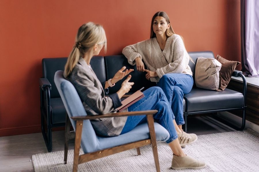 Una terapeuta y su paciente mantienen una conversación profunda en una sesión de terapia presencial, mostrando el lenguaje no verbal que la inteligencia artificial no puede captar.