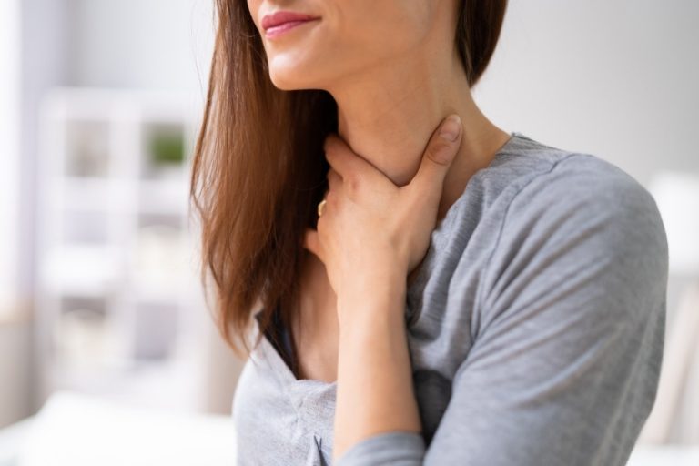 Primer plano de una mujer con la mano en el cuello, representando la sensación de cierre de garganta, dificultad para tragar o nudo en la garganta debido a la ansiedad por fagofobia.