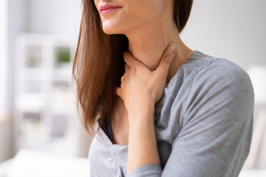 Primer plano de una mujer con la mano en el cuello, representando la sensación de cierre de garganta, dificultad para tragar o nudo en la garganta debido a la ansiedad por fagofobia.