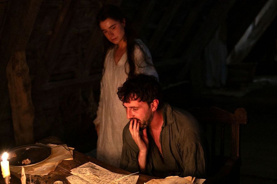 Escena de la película Hamnet: Will escribe a la luz de las velas mientras Agnes, de pie tras él, le observa en silencio