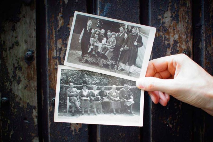 Una mano sostiene dos fotografías familiares antiguas en blanco y negro frente a una puerta oscura, representando la memoria y el trauma transgeneracional