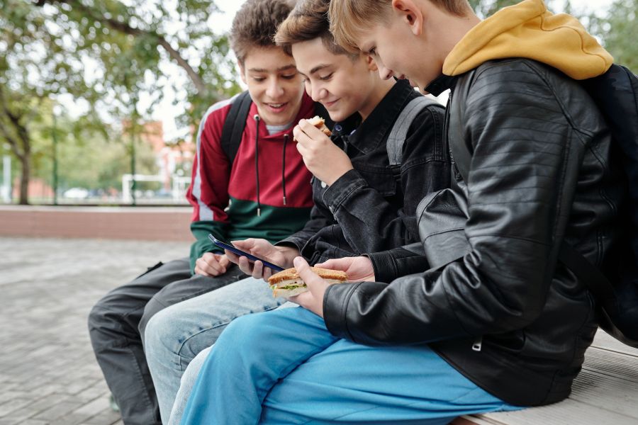 Farmear aura: tres adolescentes sentados en un banco mirando el móvil y riendo juntos, representando la dinámica de grupo y la necesidad de pertenecer en la adolescencia